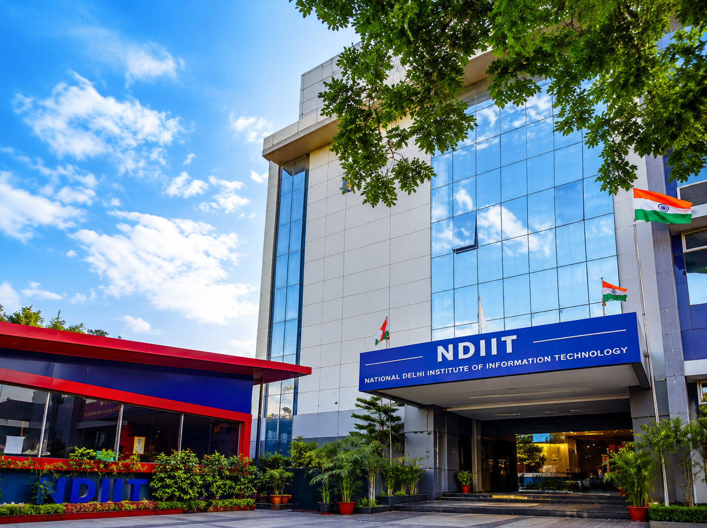 Modern NDIIT college campus building with glass exterior, Indian flags, greenery, and blue sky in Delhi.